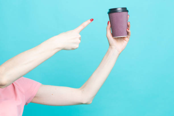 Hand of Young Caucasian Woman While Drinking Holding Cup of Coffee Over Blue Aqua Background And Pointing to Cup with Hand and Finger