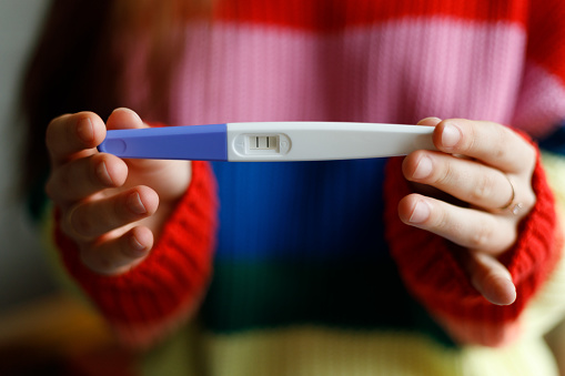 Close-up, female hands hold a positive pregnancy test with two strips.