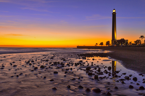 Lighthouse of Maspalomas At Gran canaria Island Known as  Faro de Maspalomas at Sunset During Blue Hour With Sea And Stones. Horizontal image Composition