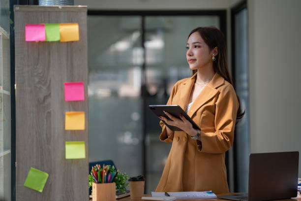 istock Asian businesswoman using a digital tablet while standing at her desk in the office. 1449100427