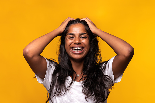 Indian happy young woman laughing touching hair with hands isolated on yellow background. Studio shot. Happiness concept.