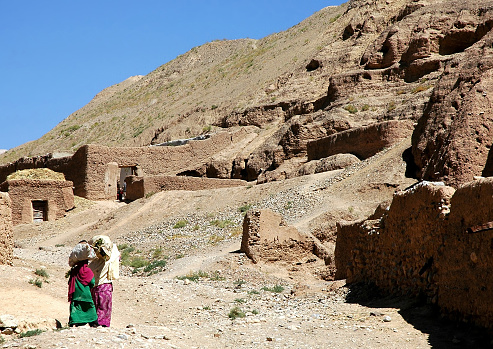 Bamyan (Bamiyan) in Central Afghanistan. A woman and girl carry goods on their heads as they walk home. These local houses are close to the Bamyan (Bamiyan) Buddhas. Local life Afghanistan. (Note: unrecognizable people)
