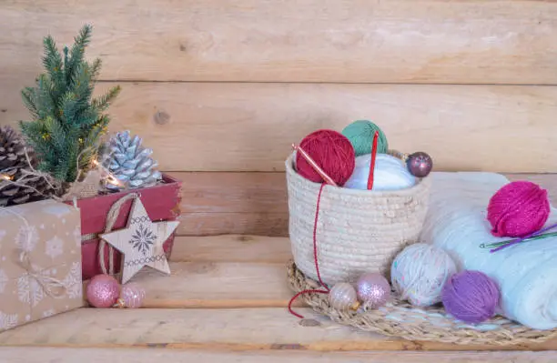 woolen colorful balls with crochet hooks in a wooden box, with christmas balls on wooden ground christmas background
