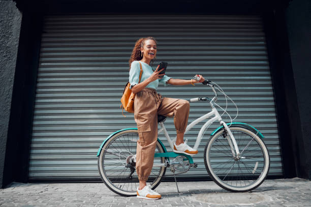 Bicycle, woman and phone in city feeling excited and happy about message while outdoor in summer with trendy look. Eco friendly transportation for carbon footprint female on a bike using 5g network bicicleta, mujer y teléfono en la ciudad sintiéndose emocionado y feliz por el mensaje mientras que al aire libre en verano con un aspecto moderno. transporte ecológico para mujeres con huella de carbono en bicicleta utilizando la red 5g