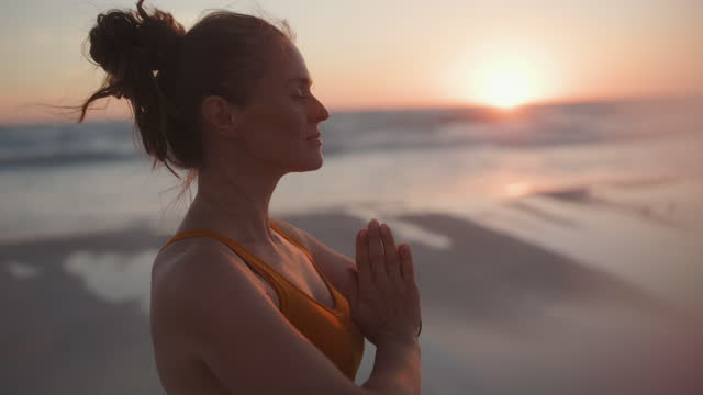 relaxed fit woman jogger at beach at sunset meditating