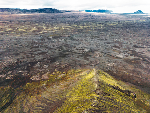 Remote volcanic lands somewhere in Iceland mainland, surrounded by vibrant green bushes and volcanic lands. Volcanic rock formations, small mountains, black grey volcanic rock. No people.