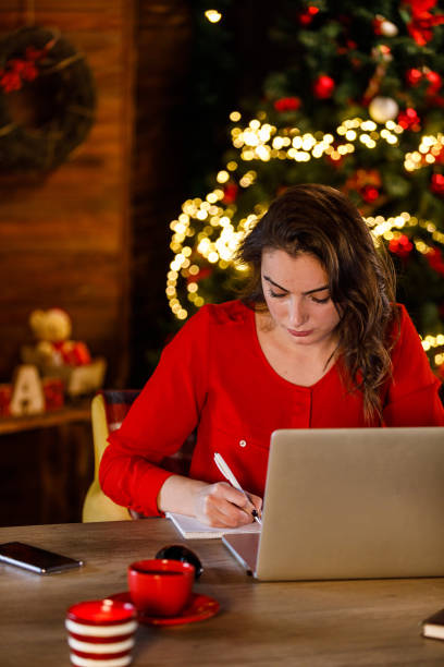 istock Young woman sitting at her desk, using laptop, working during Christmas holidays 1449124992