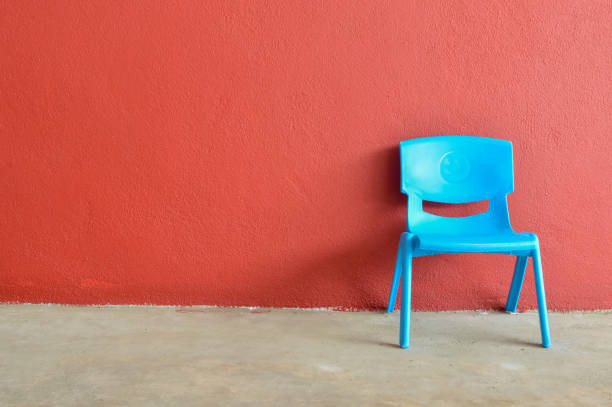 istock Blue plastic chair laid against the red wall. Copy space for the text. 1449125498