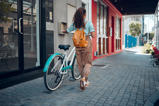 Bike, city and back view of black woman, walking on street or urban road outdoors. Exercise, fitness and female student on bicycle ride, eco friendly transportation and cycling on asphalt in town.