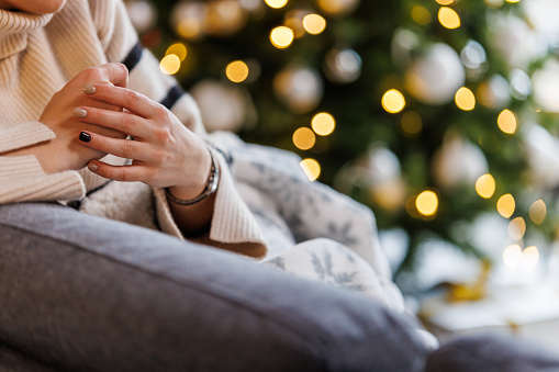 Cut out shot of distraught young woman sitting on the sofa, under a cozy, warm blanket, cracking her knuckles due to anxiety, contemplating about spending Christmas holidays alone..