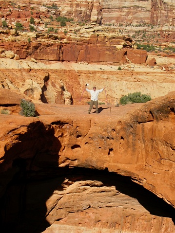 Hiker stands atop Cassidy Arch, in the Navajo sandstone high above Grand Wash in Capitol Reef National Park, Utah. Named after the infamous western outlaw Butch Cassidy (Robert Leroy Parker).