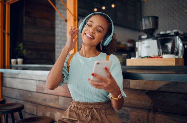 teléfono, música y cafetería con una clienta transmitiendo audio en auriculares en su cibercafé local. móvil, radio y 5g con una mujer joven usando un servicio de suscripción en un restaurante - hot drink audio fotografías e imágenes de stock