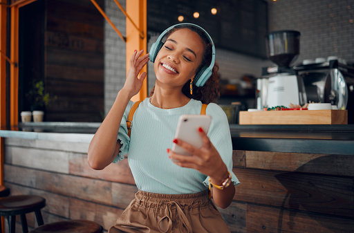 Phone, music and coffee shop with a woman customer streaming audio on headphones in her local internet cafe. Mobile, radio and 5g with a young female using a subscription service in a restaurant
