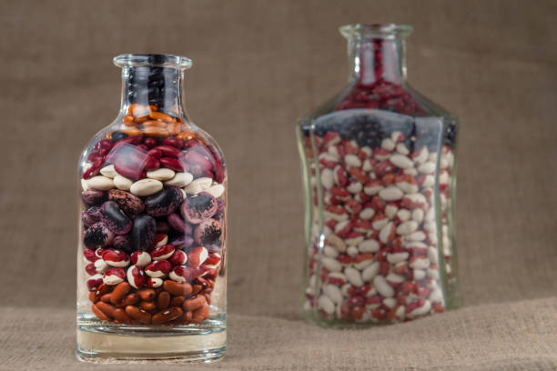 Different varieties of dry beans in glass bottles against the background of the texture of burlap.
