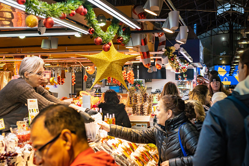 Barcelona, Spain - December 10, 2022: People shopping at Christmas time at the Boqueria market in Barcelona (Spain), selective approach to the yellow star.