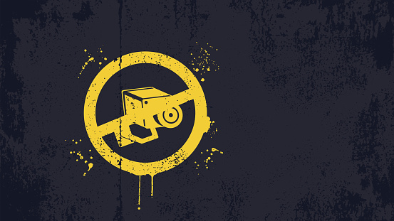 Yellow coloured no surveillance camera symbol graffiti on a dark blue grunge background