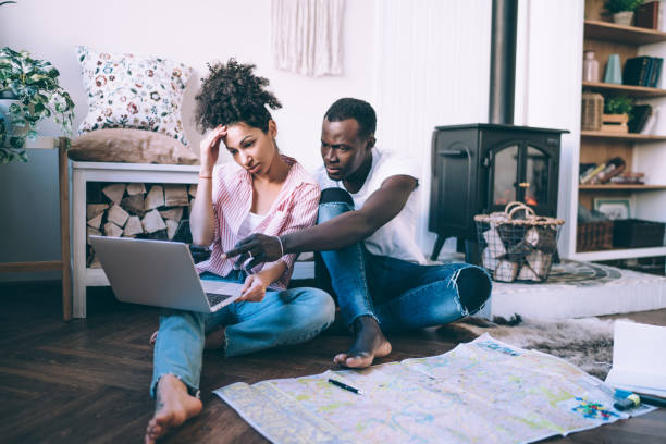 istock Multiracial couple using laptop sitting on floor with map 1449142470