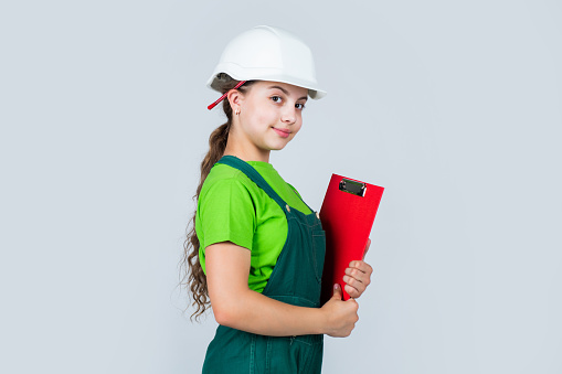 Safety expert. kid wear helmet on construction site. teen girl builder with building paper document. child on repairing work. concept of renovation in workshop. busy professional carpenter.
