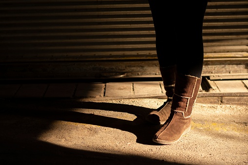 The legs of a female wearing black pants and boots and puts under a bright sunlight