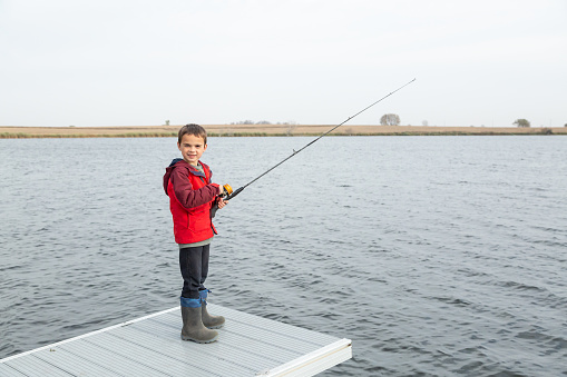 Young boy smiling at the camera while standing at the end of a dock as he fishes. Taken on an autumn day.