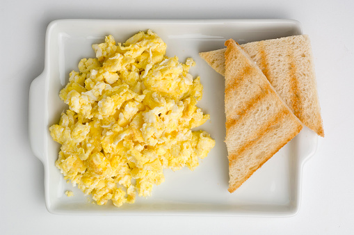 Scrambled eggs and fried bacon on plate over white stone background. Top view, flat lay