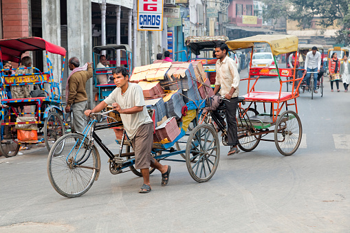 Delhi, India - January 22, 2020: Street scene, a cyclist carrying goods through the downtown Delhi, India.