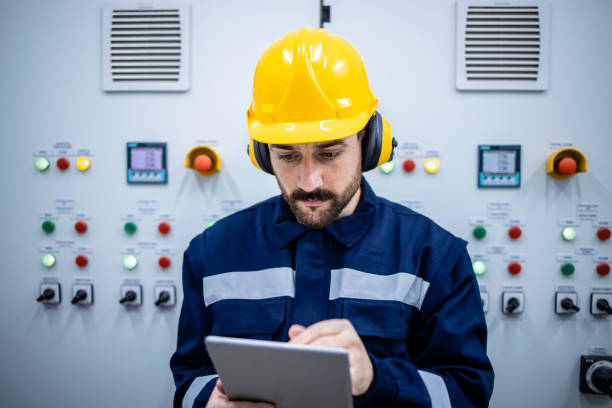 istock Industrial electric engineer checking voltage and power on his diagnostic tool while standing by electrical cabinet inside factory. 1449161540