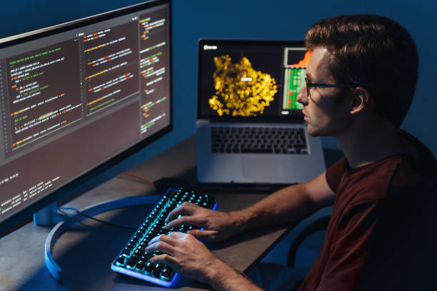 Closeup of program developer writing software on multiple computer screens at home office Profile closeup view of young handsome program developer writing software on multiple computer screens at home office. IT specialist, data scientist, coding concept python stock pictures, royalty-free photos & images