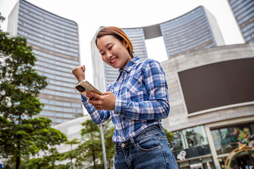 Beautiful Asian businesswoman in a financial area, holding a smartphone.