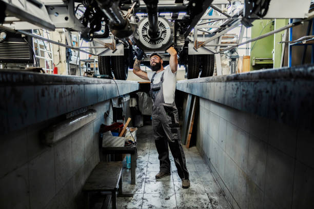 An auto-mechanic in a pit looking at broken vehicle and trying to fix it.