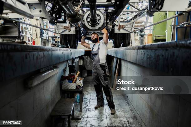 An Automechanic In A Pit Looking At Broken Vehicle And Trying To Fix It Stock Photo - Download Image Now