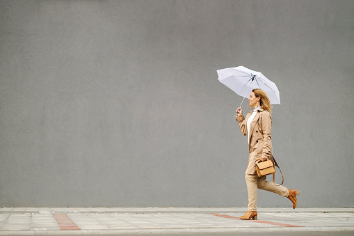 A woman in heels is running on the street on a rainy autumn day and running from rain.