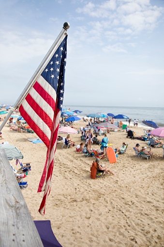 American Flag looks over Crowds of people having fun at the beach.