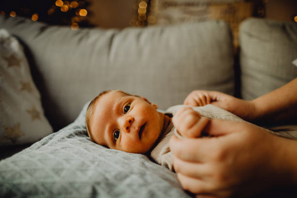 Portrait of a newborn baby boy laying on the bed and looking at the camera Close-up portrait of a newborn baby boy laying on the bed while his unrecognizable mother is holding his hands. emotion regulation in babies stock pictures, royalty-free photos & images