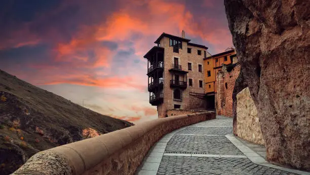 sunset with a view of the Hanging Houses of Cuenca, Spain, with a rock, a sky with blue, orange and pink clouds, and a landscape of the city - tourist postcard or wallpaper of the city of Castilla