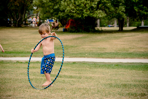 There is a three year old boy just learning how to use a hulahoop and trying his best