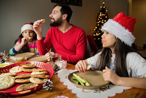 Middle eastern family having a festive breakfast. They are having tea and manakish, a traditional bread made with cheese and Zaatar. Little girls are wearing festive Santa’s hat. Horizontal waist up indoors shot. This was taken in Montreal, Quebec, Canada.