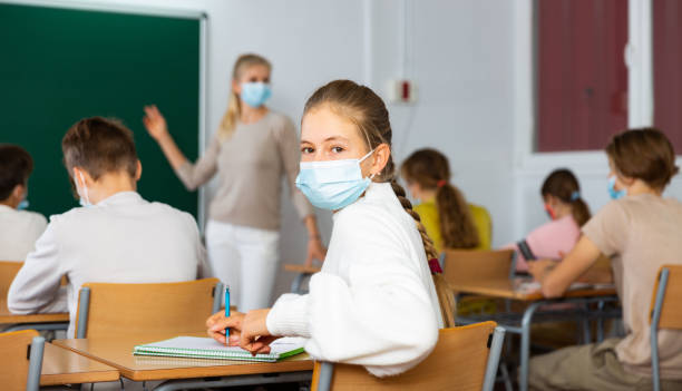 istock Student in protective mask studying in classroom, listening to lecturer and writing in notebook 1449191510