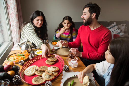 Middle eastern family having a festive breakfast. They are having tea and manakish, a traditional bread made with cheese and Zaatar. Little girls are 9 and 10 year’s old. Horizontal waist up indoors shot. This was taken in Montreal, Quebec, Canada.