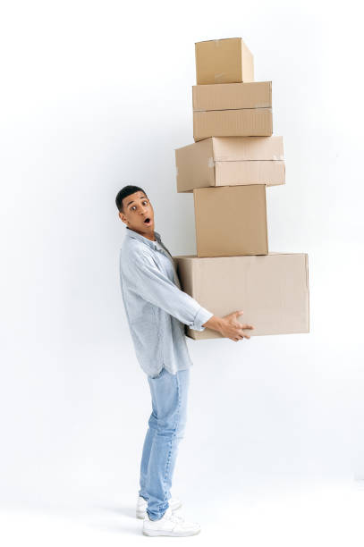 istock Stunned mixed race guy in casual stylish clothes, delivery man, standing over isolated white background, holding many cardboard boxes, delivering parcels, looking in amazement at camera, delivery 1449201421