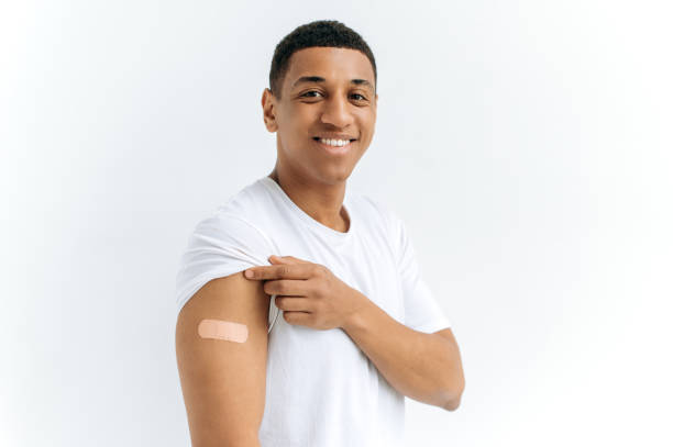 istock Mixed race happy guy stands on isolated white background with a plaster on his shoulder, received a vaccine against various diseases, looks at the camera, smiles. Healthcare and immunity concept 1449201635