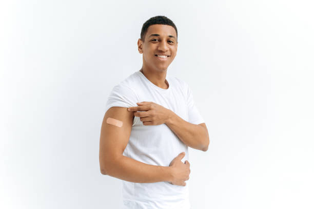 istock Mixed race handsome guy, stands on an isolated white background with a plaster on his shoulder, received a vaccine against various diseases, acquired immunity, looks at the camera, smiles happily 1449201643