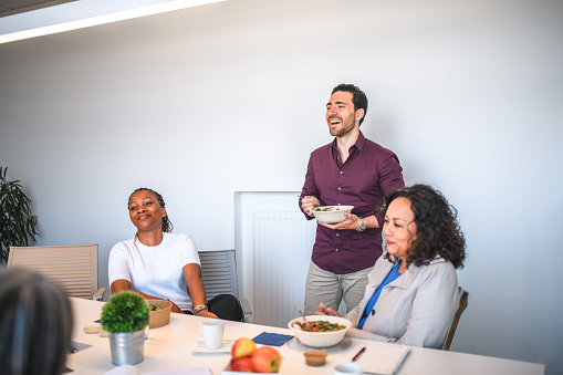 Fun portrait of African American, Hispanic and Caucasian employees. They are enjoying a vegetarian lunch at office desk.