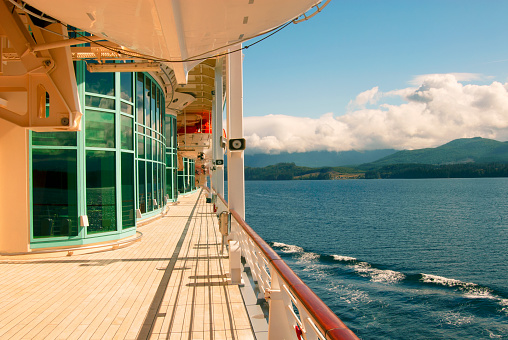 The side of a generic cruise ship sailing along a coastline on a sunny day