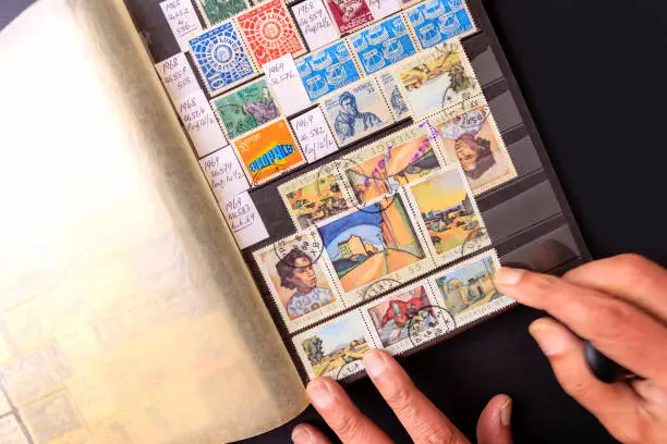 Hands of a collector arranging a page in his stock album showing Swedish stamps. They have been placed under cellophane strips which protects the stamps. The page has the collector's handwritten notes including dates of issue. They are all commemorative issues and have been cancelled. Swedish postage stamps have a reputation of good design and execution. Collector's Property Release available.