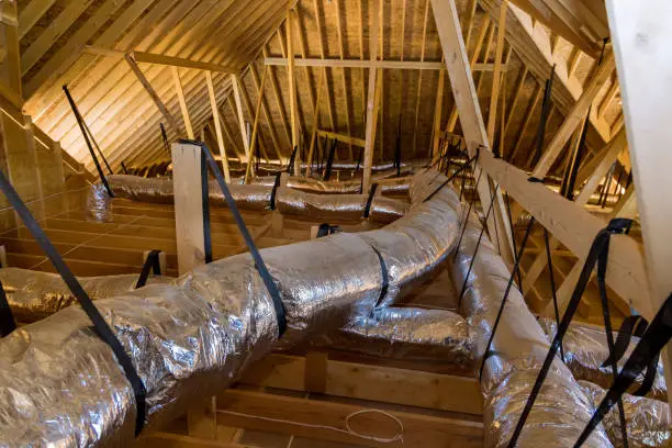 Photo of In a newly built home under construction, ventilation pipes are found in the silver insulation material on the ceiling of the attic