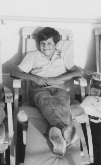 Image taken in the 60s: Smiling boy looking at the camera sitting at a cruise deck