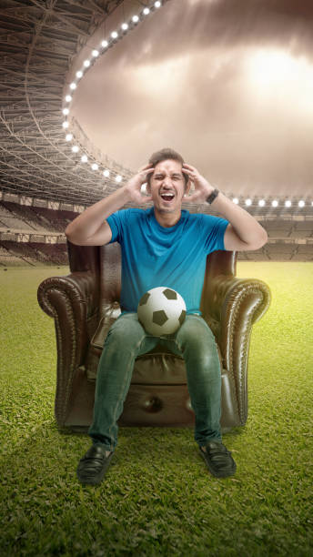 istock Asian man with the ball sitting on the couch with a disappointed expression 1449246542