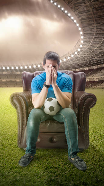 istock Asian man with the ball sitting on the couch with a disappointed expression 1449246569