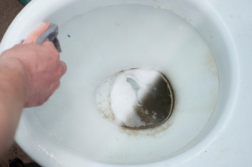 The process of cleaning an old dirty toilet bowl with different detergents and a washcloth in hand